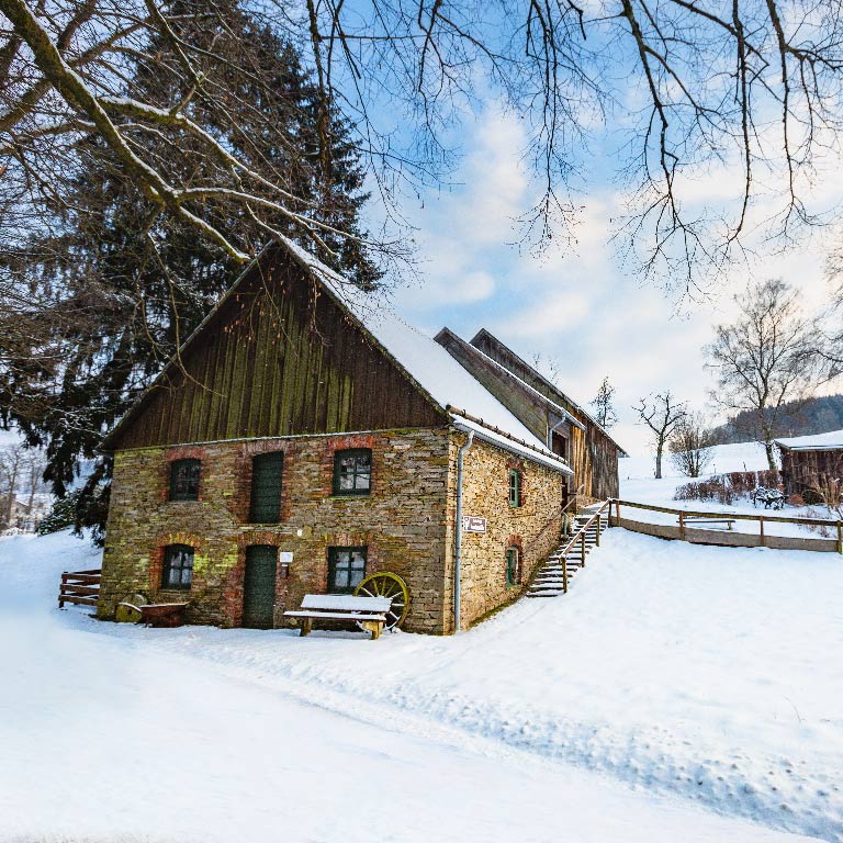 Das Bild zeigt ein altes Gebäude. Es ist die Knochenmühle. Es liegt Schnee. Die Knochenmühle steht in der Natur